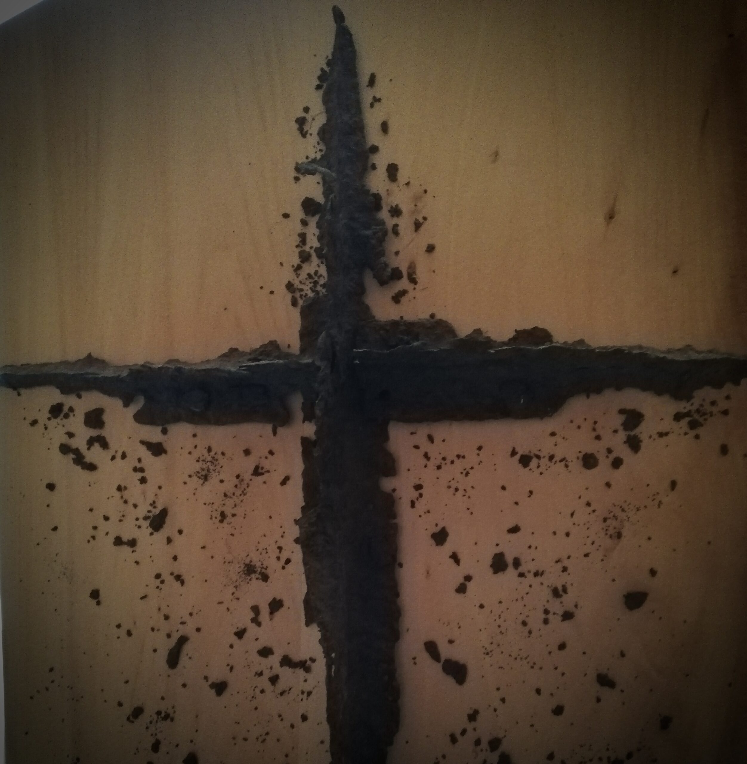 Ein Kreuz aus rostigem Eisen auf einer Holzplatte