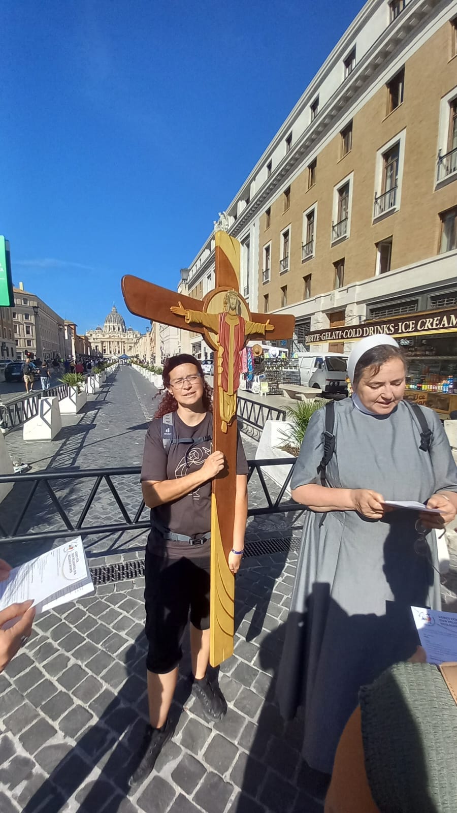 Eine Person die das Kreuz des Heiligen Jahres trägt und eine Person, die einen Text vorliest.
